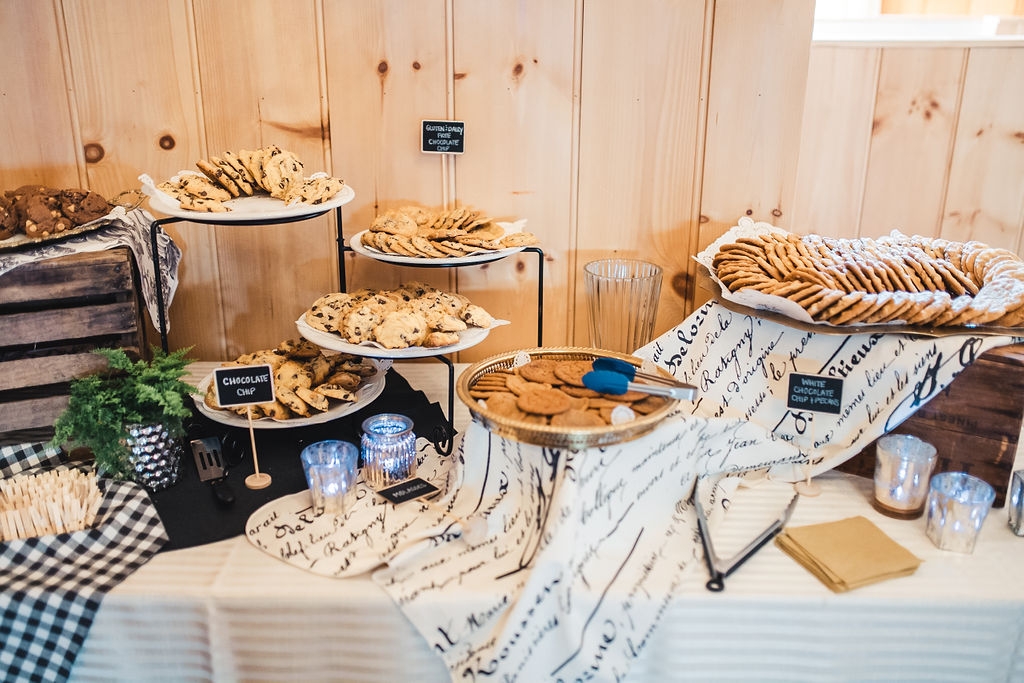 A table covered in linens and trays full of various cookies at a Melhorn Manor event